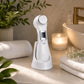 Full view of the 6-in-1 Beauty Device standing upright on a minimalist bathroom shelf, surrounded by towels and botanicals, highlighting its compact and sophisticated appearance.