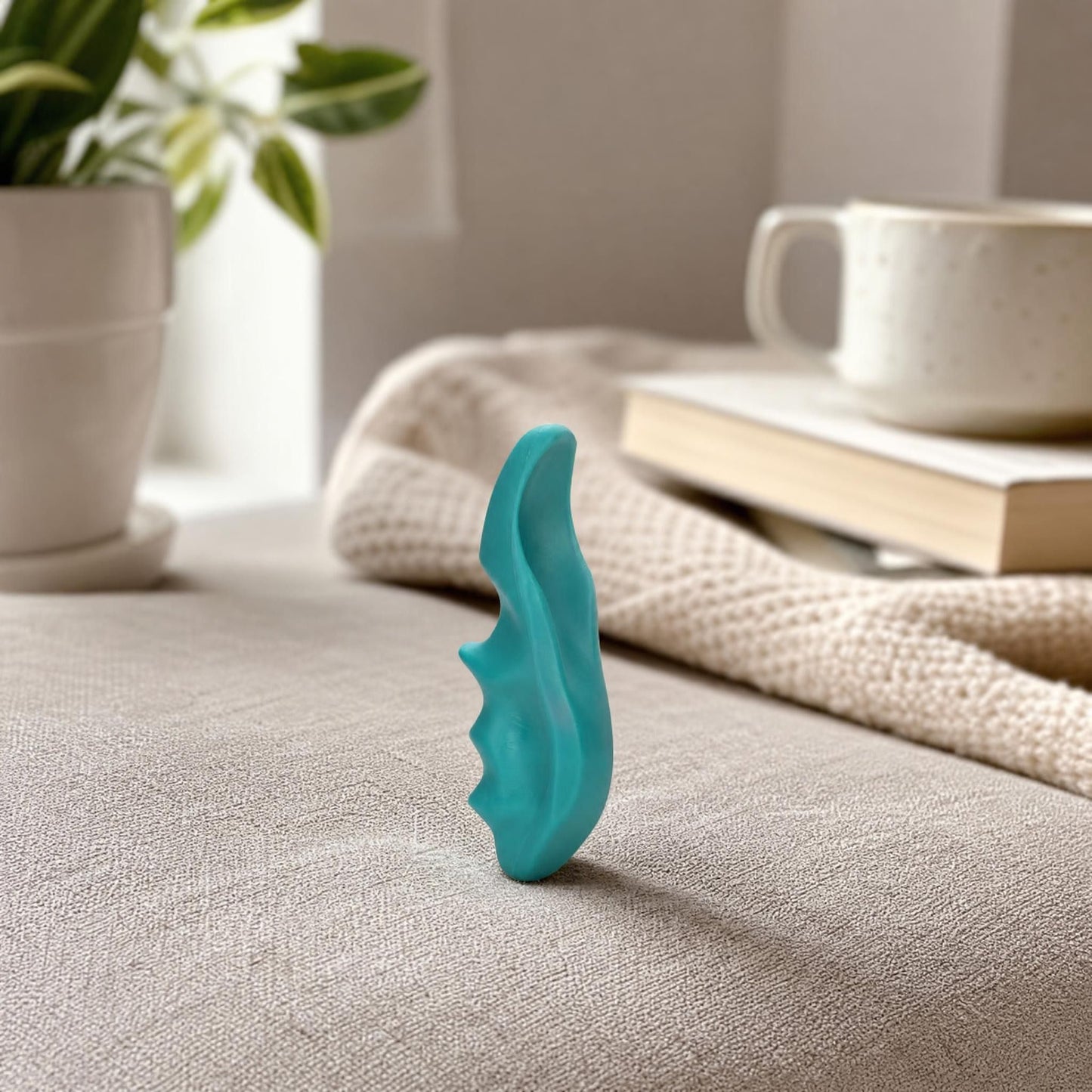 Side view of a lightweight trigger point massager on fabric, showing ergonomic curves and textured grip in a cozy home setting.