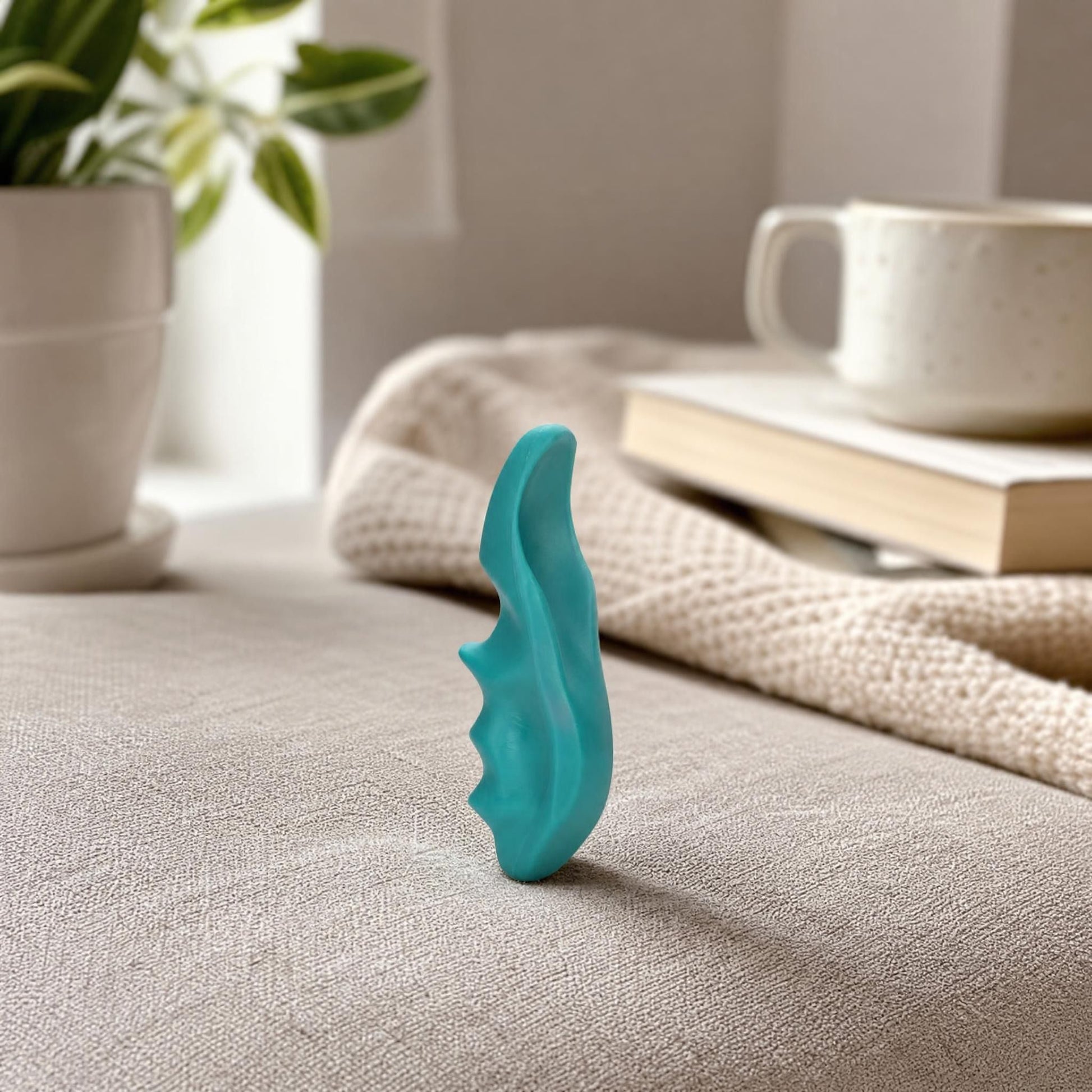 Side view of a lightweight trigger point massager on fabric, showing ergonomic curves and textured grip in a cozy home setting.
