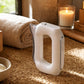 Gua sha massager on jute mat with ambient candlelight, among wellness accessories in a rustic bathroom setting.