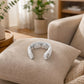 The SKG Smart Neck Massager resting on a fabric cushion in a cozy living room, showcasing its ergonomic design and portability.