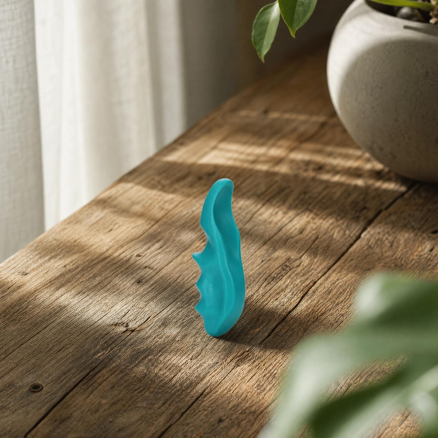 Close-up of a small ergonomic trigger point massager on a wooden surface, highlighting its contours and textured grip.